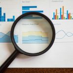 A magnifying glass focuses on various business charts and graphs on paper.